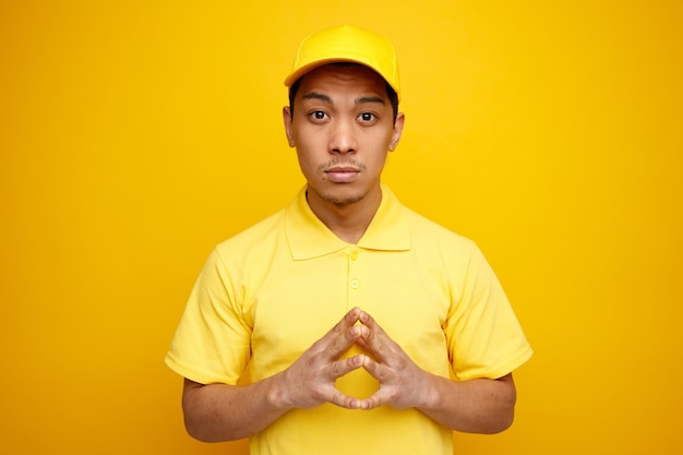 Repartidor joven pensativo con gorra y uniforme manteniendo las manos juntas