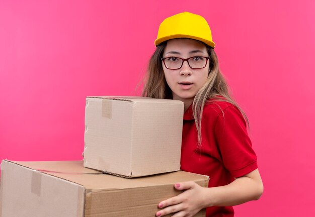 Repartidor joven en polo rojo y gorra amarilla sosteniendo