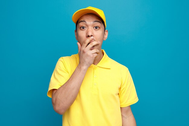 Repartidor joven preocupado vestido con uniforme y gorra haciendo gesto Uy