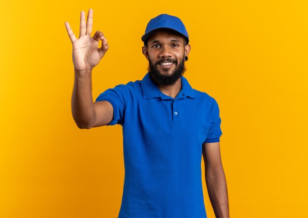 Repartidor joven sonriente gesticulando ok firmar aislado en la pared naranja con espacio de copia