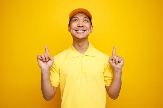 Repartidor joven sonriente con gorra y uniforme mirando y apuntando hacia arriba