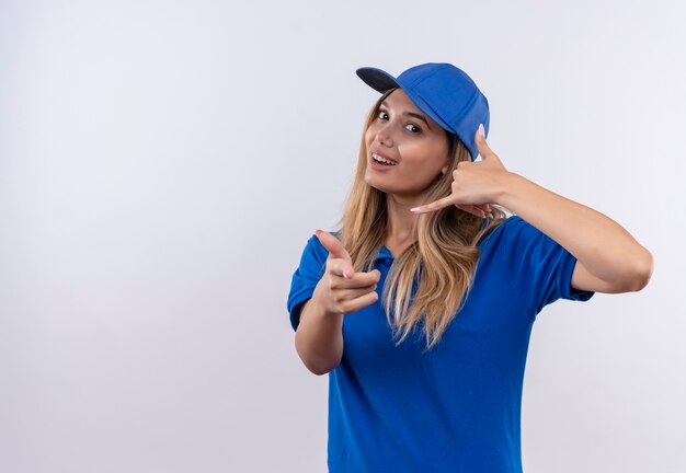 Repartidor joven sonriente con uniforme azul y gorra mostrando gesto de llamada telefónica y gesto aislado en blanco