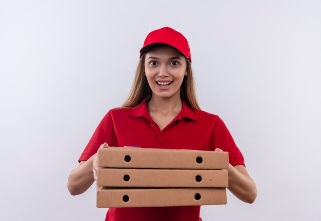 Repartidor joven sonriente con uniforme rojo y gorra con caja de pizza aislado en blanco