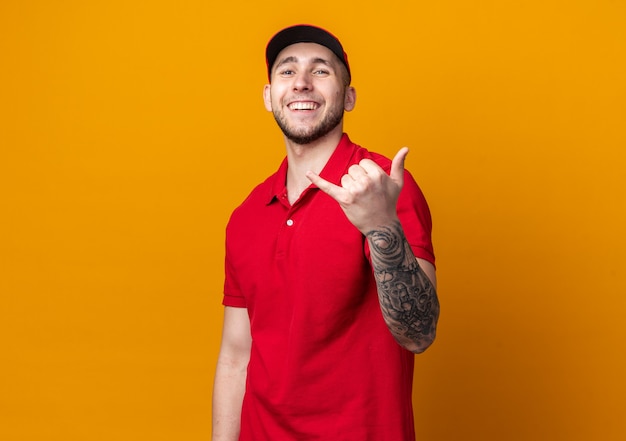 Repartidor joven sonriente vistiendo uniforme con gorra mostrando gesto de llamada telefónica