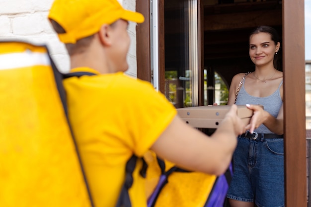 Repartidor joven en uniforme amarillo ofrece orden a los clientes idea de comodidad velocidad comodidad