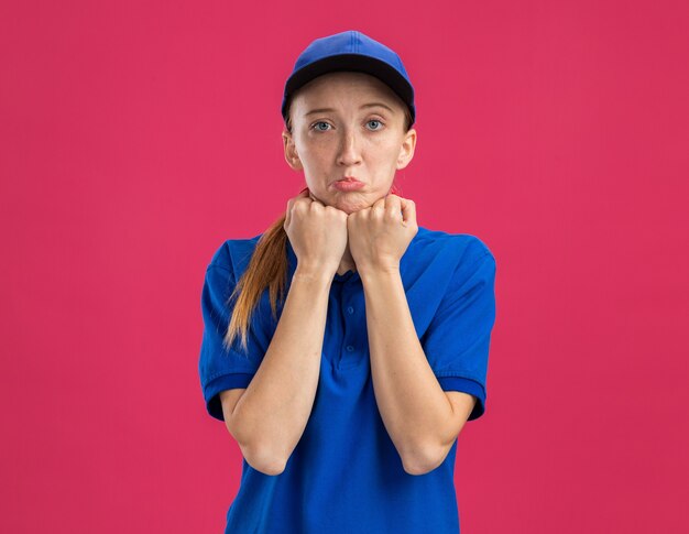 Repartidor joven en uniforme azul y gorra con expresión triste frunciendo los labios