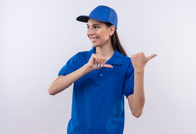 Repartidor joven en uniforme azul y gorra hapy y positivo apuntando con los dedos hacia un lado