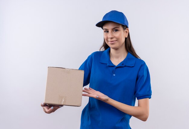 Repartidor joven en uniforme azul y gorra con paquete de caja sonriendo confiado