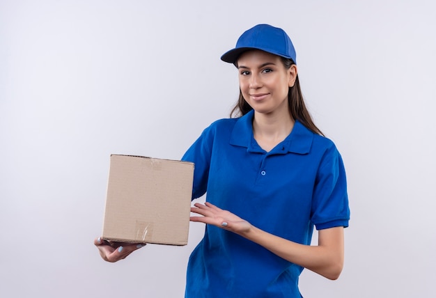 Repartidor joven en uniforme azul y gorra con paquete de caja sonriendo confiado