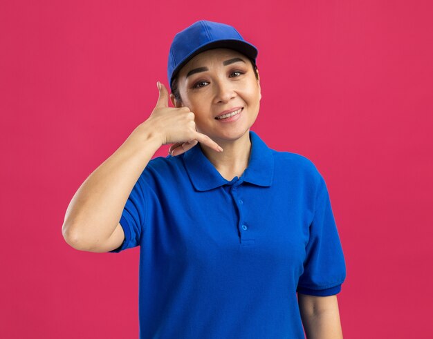 Repartidor joven en uniforme azul y gorra sonriendo alegremente haciendo gesto de llamarme