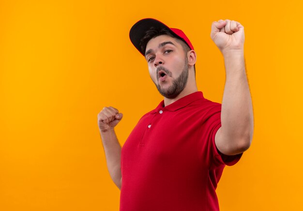 Repartidor joven en uniforme rojo y gorra apretando los puños feliz y salido