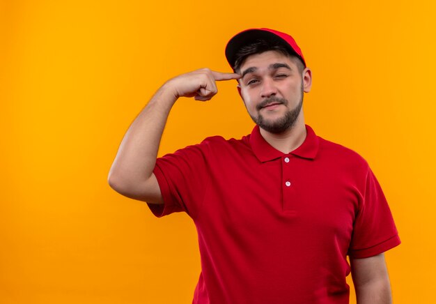 Repartidor joven en uniforme rojo y gorra apuntando su templo centrado en la tarea