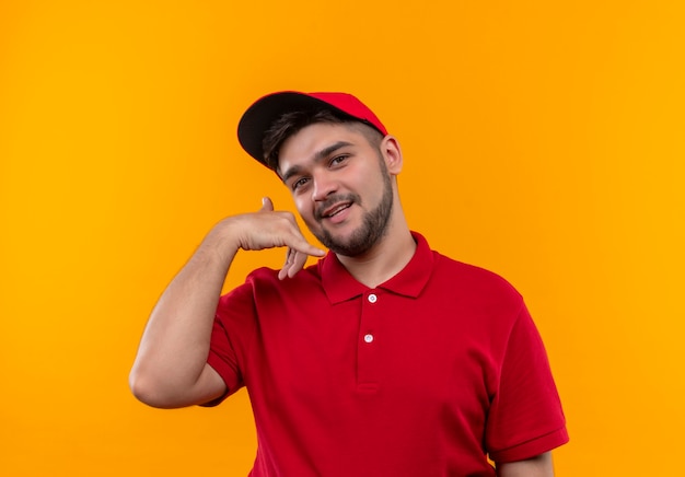 Repartidor joven en uniforme rojo y gorra haciendo gesto de llamarme con una sonrisa en la cara