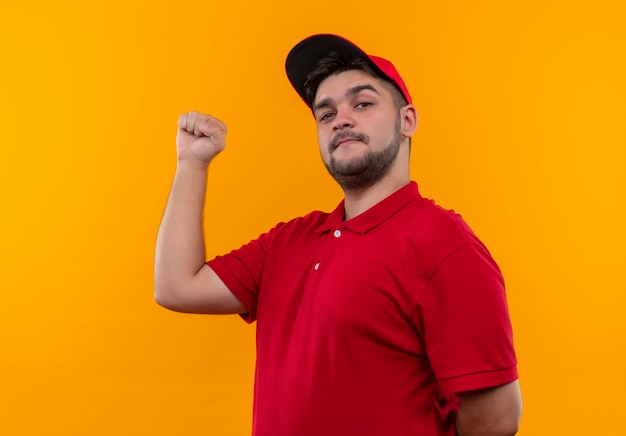 Repartidor joven en uniforme rojo y gorra mirando confiado y orgulloso levantando el puño