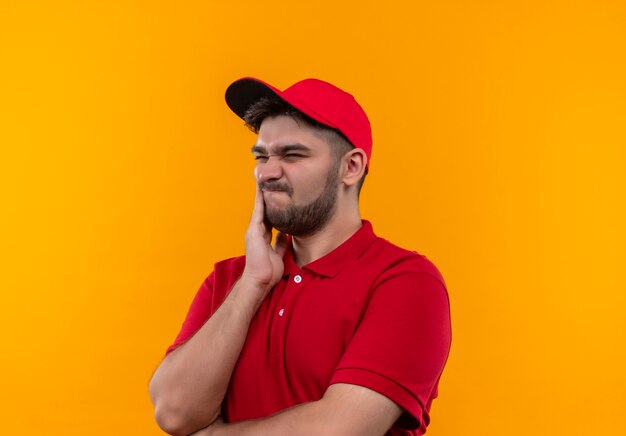 Repartidor joven en uniforme rojo y gorra mirando a un lado confundido y muy ansioso