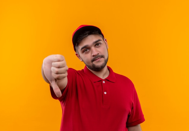 Repartidor joven en uniforme rojo y gorra mostrando los pulgares hacia abajo con cara infeliz