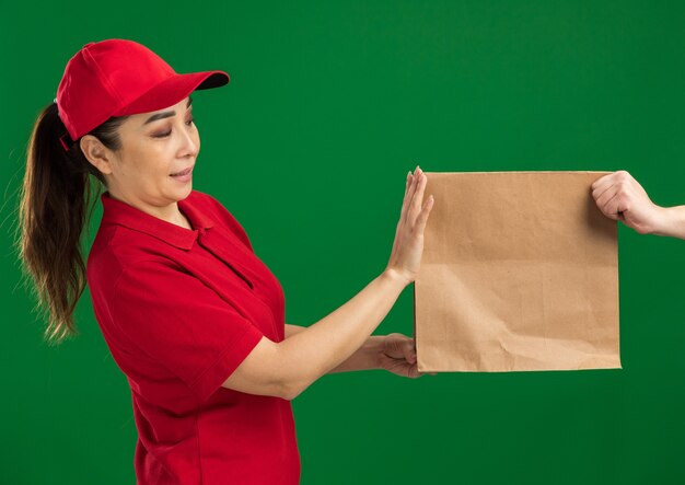 Repartidor joven en uniforme rojo y gorra negándose a recibir paquete de papel