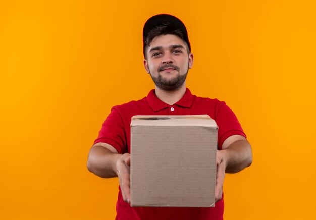 Repartidor joven en uniforme rojo y gorra con paquete de caja sonriendo confiado
