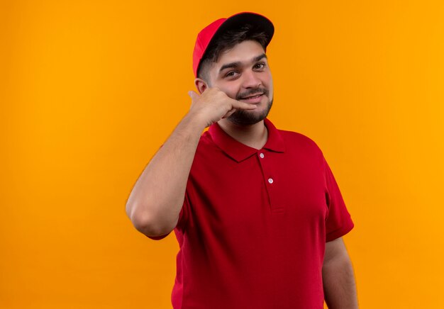 Repartidor joven en uniforme rojo y gorra sonriendo maning llámame gesto