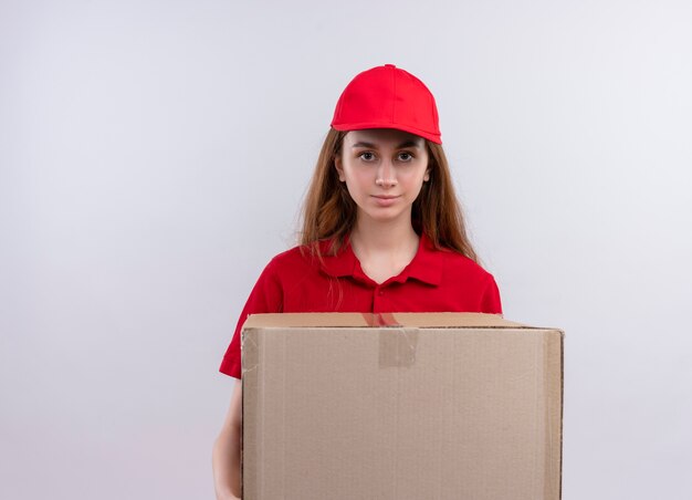 Repartidor joven en uniforme rojo sosteniendo la caja y en la pared blanca aislada con espacio de copia