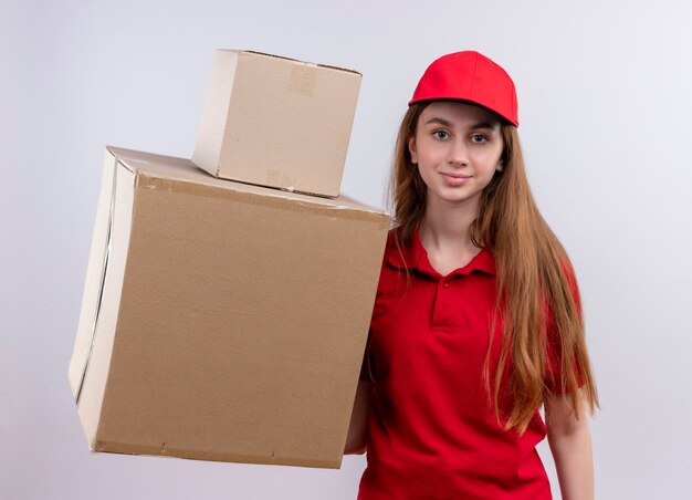 Repartidor joven en uniforme rojo sosteniendo cajas en pared blanca aislada