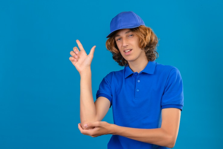 Foto gratuito repartidor joven vestido con camisa polo azul y gorra apuntando con la mano y el dedo hacia el lado sonriendo de pie sobre aislado