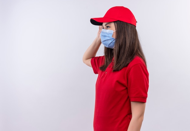 Repartidor joven vistiendo camiseta roja en gorra roja lleva mascarilla sobre fondo blanco aislado