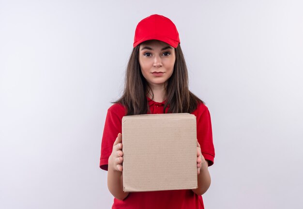 Repartidor joven vistiendo camiseta roja en gorra roja sosteniendo una caja sobre fondo blanco aislado