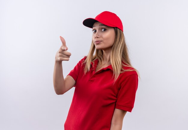 Repartidor joven vistiendo uniforme rojo y gorra mostrando gesto de pistola aislado en la pared blanca