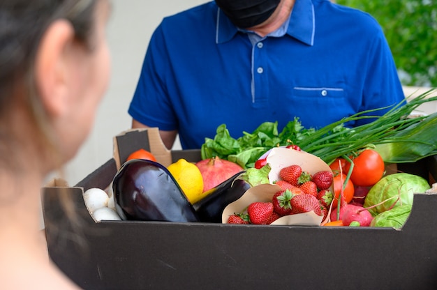 Repartidor con una máscara facial y sosteniendo una caja con verduras