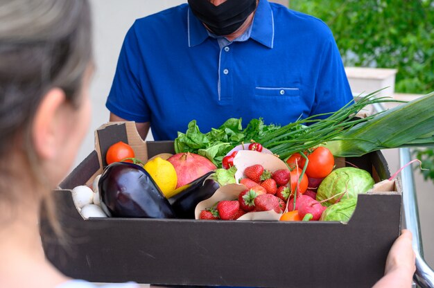 Repartidor con una máscara facial y sosteniendo una caja con verduras