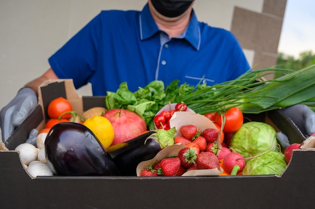 Repartidor con una máscara facial y sosteniendo una caja con verduras