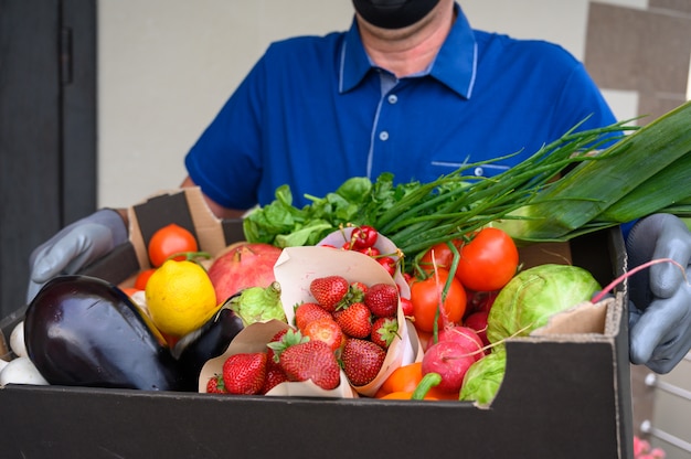 Repartidor con una máscara facial y sosteniendo una caja con verduras