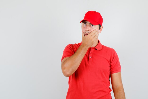 Repartidor mirando hacia arriba con la mano en la cara en camiseta roja
