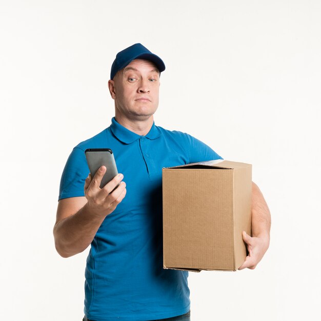 Repartidor mirando sorprendido al teléfono mientras sostiene una caja de cartón