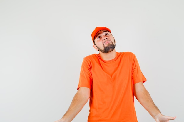 Foto gratuita repartidor mostrando gesto de impotencia encogiéndose de hombros en camiseta naranja, gorra y mirando confundido. vista frontal.