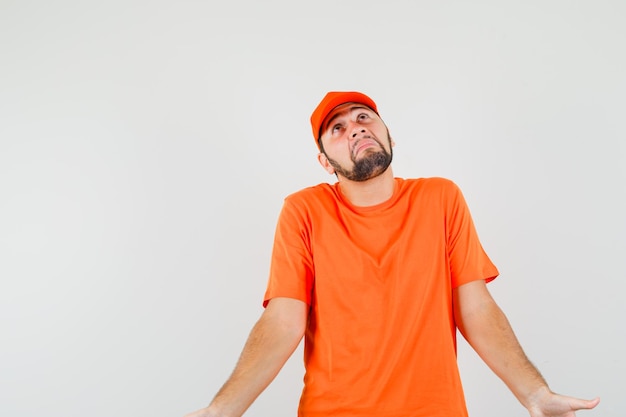 Repartidor mostrando gesto de impotencia encogiéndose de hombros en camiseta naranja, gorra y mirando confundido. vista frontal.