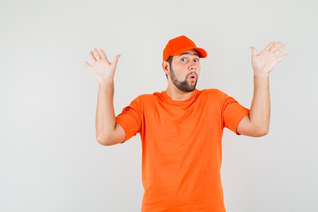 Repartidor mostrando gesto de rendición en camiseta naranja, gorra, vista frontal.