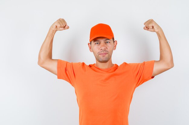 Repartidor mostrando los músculos de los brazos en camiseta naranja y gorra y luciendo fuerte