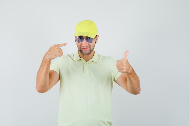 Repartidor mostrando el pulgar hacia arriba apuntando a las gafas con uniforme amarillo y luciendo orgulloso, vista frontal.