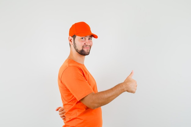 Repartidor mostrando el pulgar hacia arriba en camiseta naranja, gorra y mirando alegre. vista frontal.