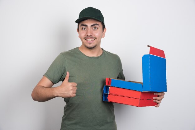 Repartidor mostrando los pulgares hacia arriba y llevando cajas de pizza sobre fondo blanco.
