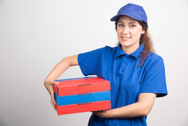 Repartidor de pizzas llevando tres cajas sobre fondo blanco.