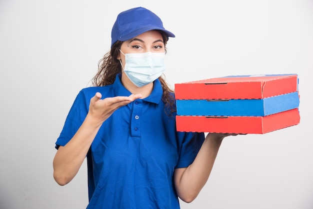 Repartidor de pizzas sosteniendo tres cajas con mascarilla médica en blanco