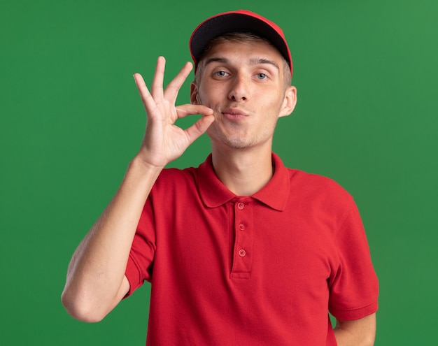 Foto gratuita repartidor rubio joven confiado finge cerrar la boca en verde