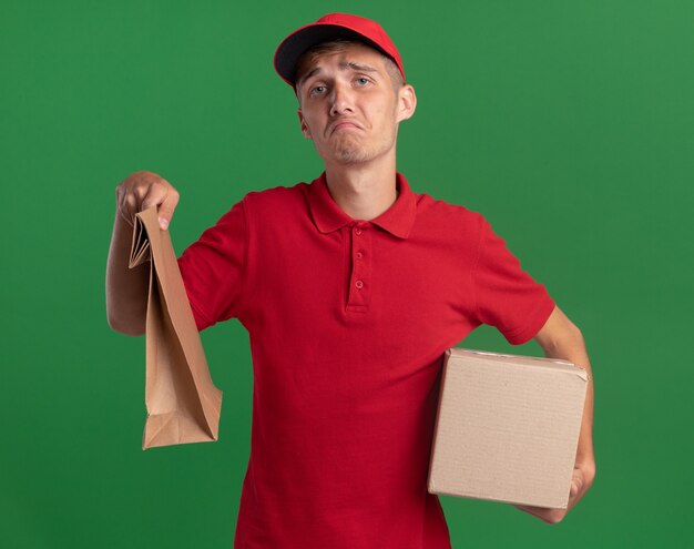 Repartidor rubio joven decepcionado sostiene el paquete de papel y la caja de cartón en verde