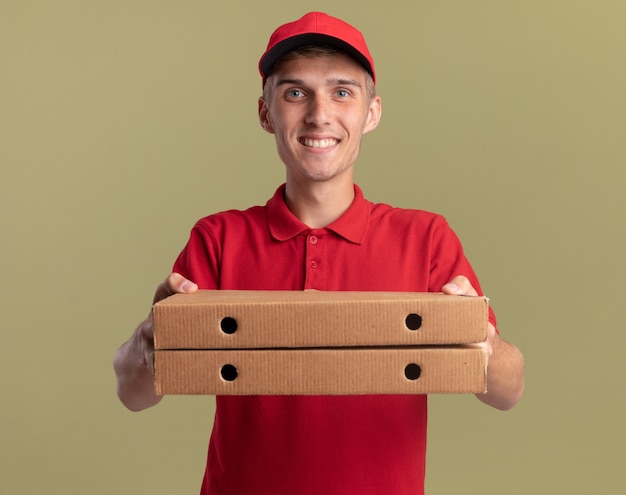 Repartidor rubio joven sonriente sosteniendo cajas de pizza en verde oliva