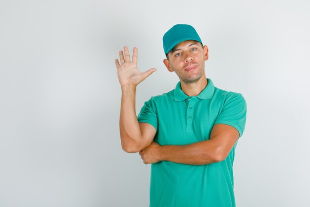 Repartidor saludo con mano abierta en camiseta verde con gorra