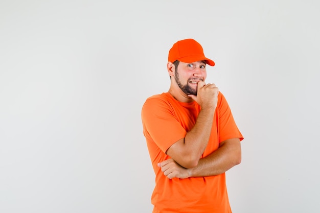 Repartidor se siente incómodo mientras está en camiseta naranja, gorra y parece emocionado, vista frontal.