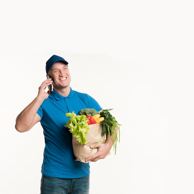 Repartidor sonriente hablando por teléfono mientras llevaba una bolsa de supermercado